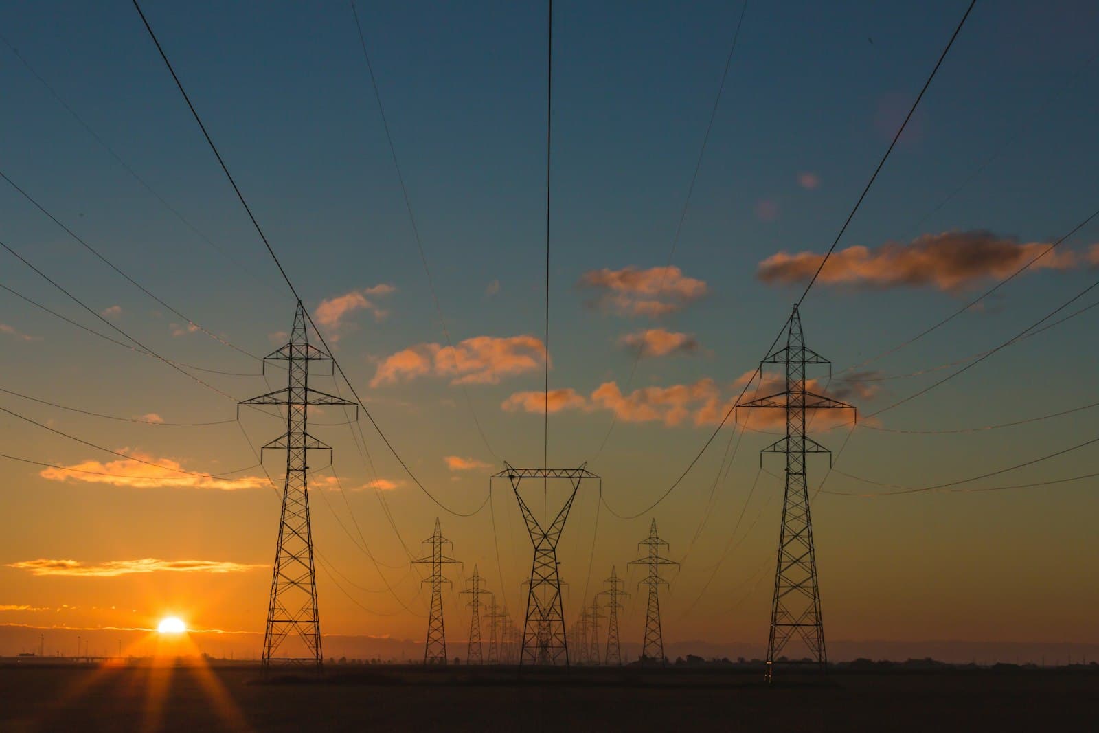 High-voltage transmission towers across open land at sunset