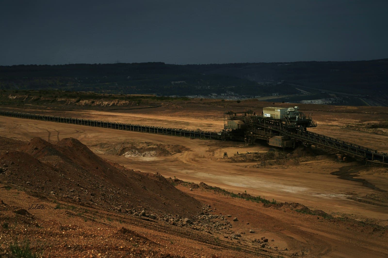Conveyor system crossing an open-pit mining site under a dark sky